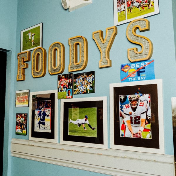 Foodys sign and framed sports memorabilia, including Tom Brady, on a light blue wall.
