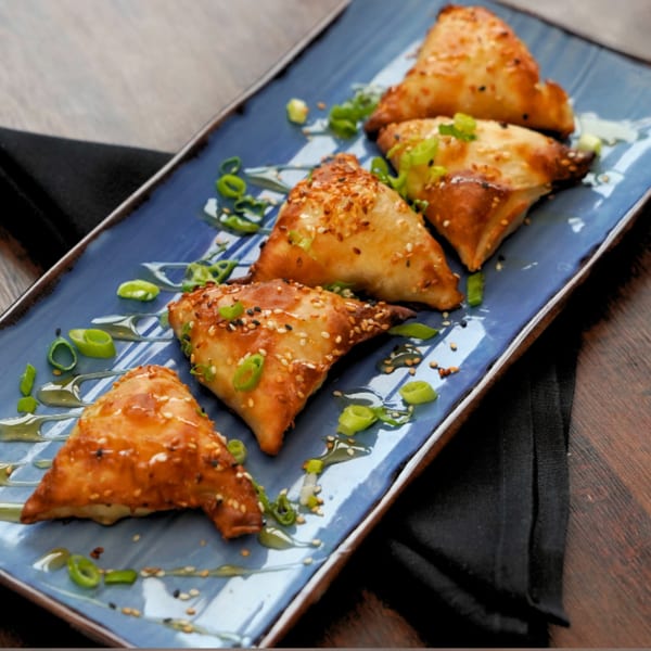 Golden-brown samosas with sesame seeds and green onions on a blue rectangular plate at Foodys Tampa.