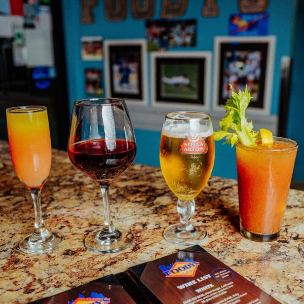 Four drinks, including a mimosa, red wine, Stella Artois beer, and a Bloody Mary, on a bar.
