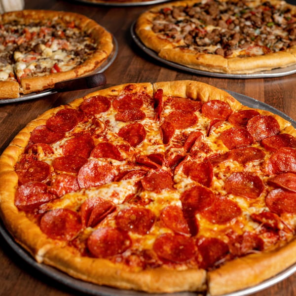 Three pizzas on metal trays, with a large pepperoni pizza in the foreground.