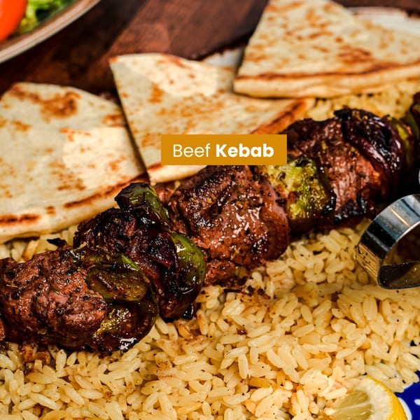 Grilled beef kebab with green peppers, served over rice with pita bread and a lemon wedge.
