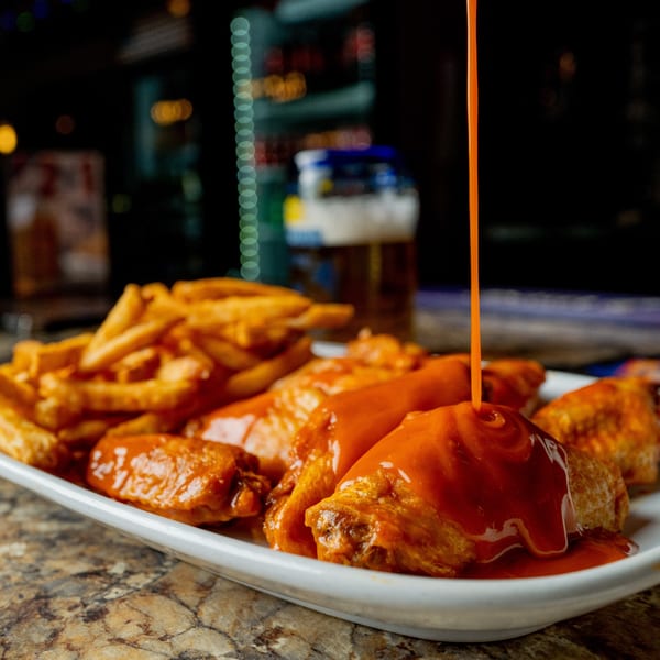 Buffalo sauce pouring over crispy chicken wings and a side of golden fries at Foodys Tampa.