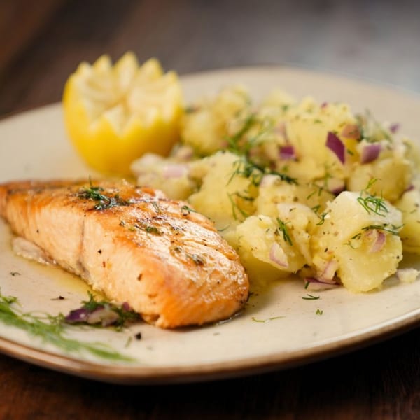 Grilled salmon fillet with a side of potato salad, garnished with dill and a lemon wedge.