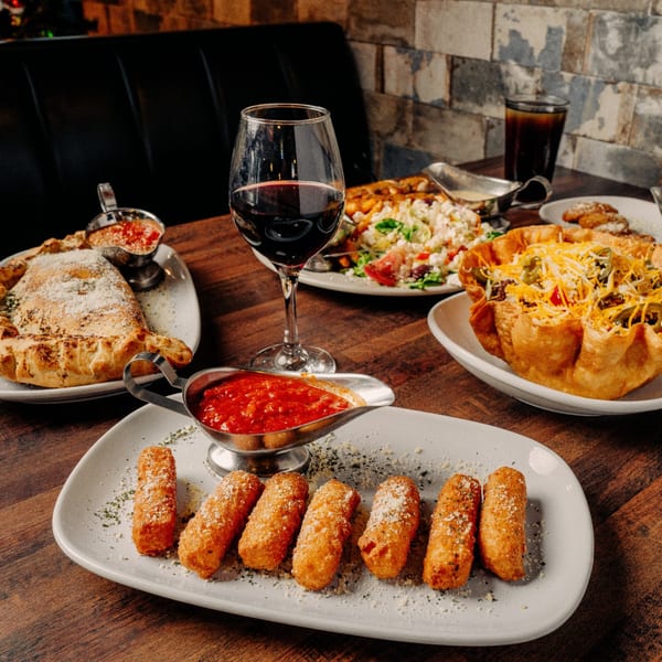 A table at Foodys Tampa laden with mozzarella sticks, calzone, taco salad, and a glass of red wine.