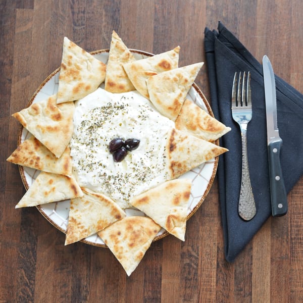 A plate of Foodys Tampa's tzatziki dip with pita bread, garnished with olives and herbs.