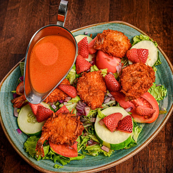 Foodys Tampa's coconut shrimp salad with strawberries, cucumbers, tomatoes, and a side of dressing.